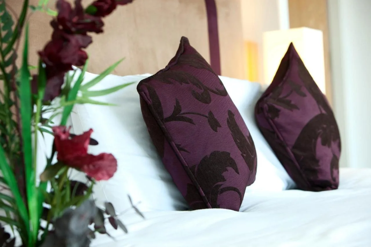 two purple pillows sitting on a bed with flowers at The Spires Serviced Apartments Glasgow in Glasgow