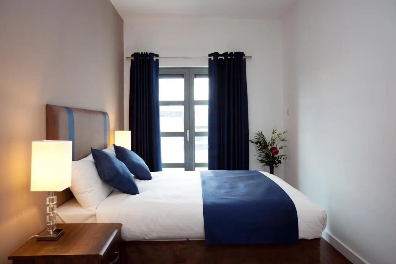 a bedroom with a bed with blue pillows and a window at The Spires Serviced Apartments Glasgow in Glasgow