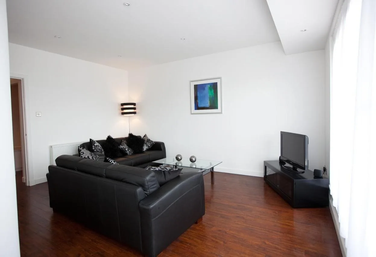 a living room with a black couch and a tv at The Spires Serviced Apartments Glasgow in Glasgow