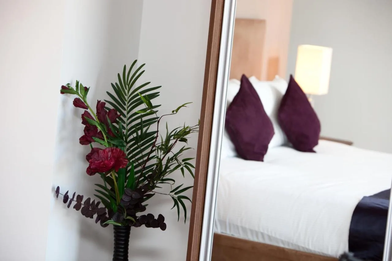 a mirror and a vase with flowers in front of a bedroom at The Spires Serviced Apartments Glasgow in Glasgow